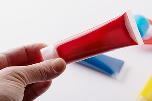 Close-up of a hand holding a red paint tube with blurred blue an, a Holiday Photo by Ales Munt