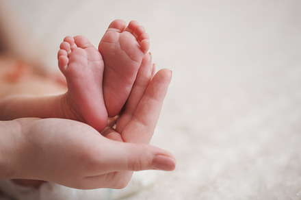 Mother holds little foot of newborn baby featuring baby, mother, and feet