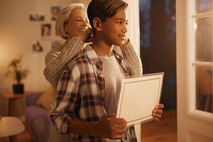 Young man holding blank sign while mother puts necklace, a Photo by DanFLCreativo