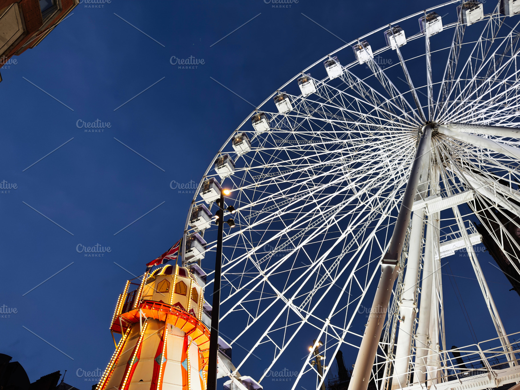 Manchester Ferris wheel at night beside illuminated tower and glowing city ligh, a Photo by AS photostudio