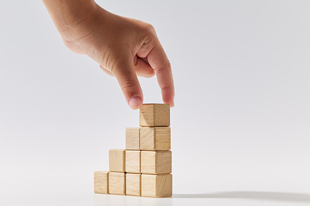 Hand putting wood cubes stacked as stair step shapes on white, a Business Photo by 1981 Rustic studio kan