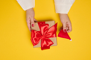 Two female hands in a white knitted sweater hold a square gift b, a Holiday Photo by ndanko