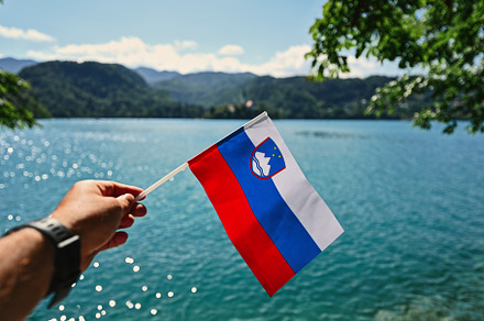 Man hand hold slovenian flag against view of beautiful Bled Lake, a Photo by AS photostudio