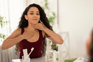 Beautiful young woman making lymphatic drainage neck self massage in front of m, a Photo by Prostock-Studio