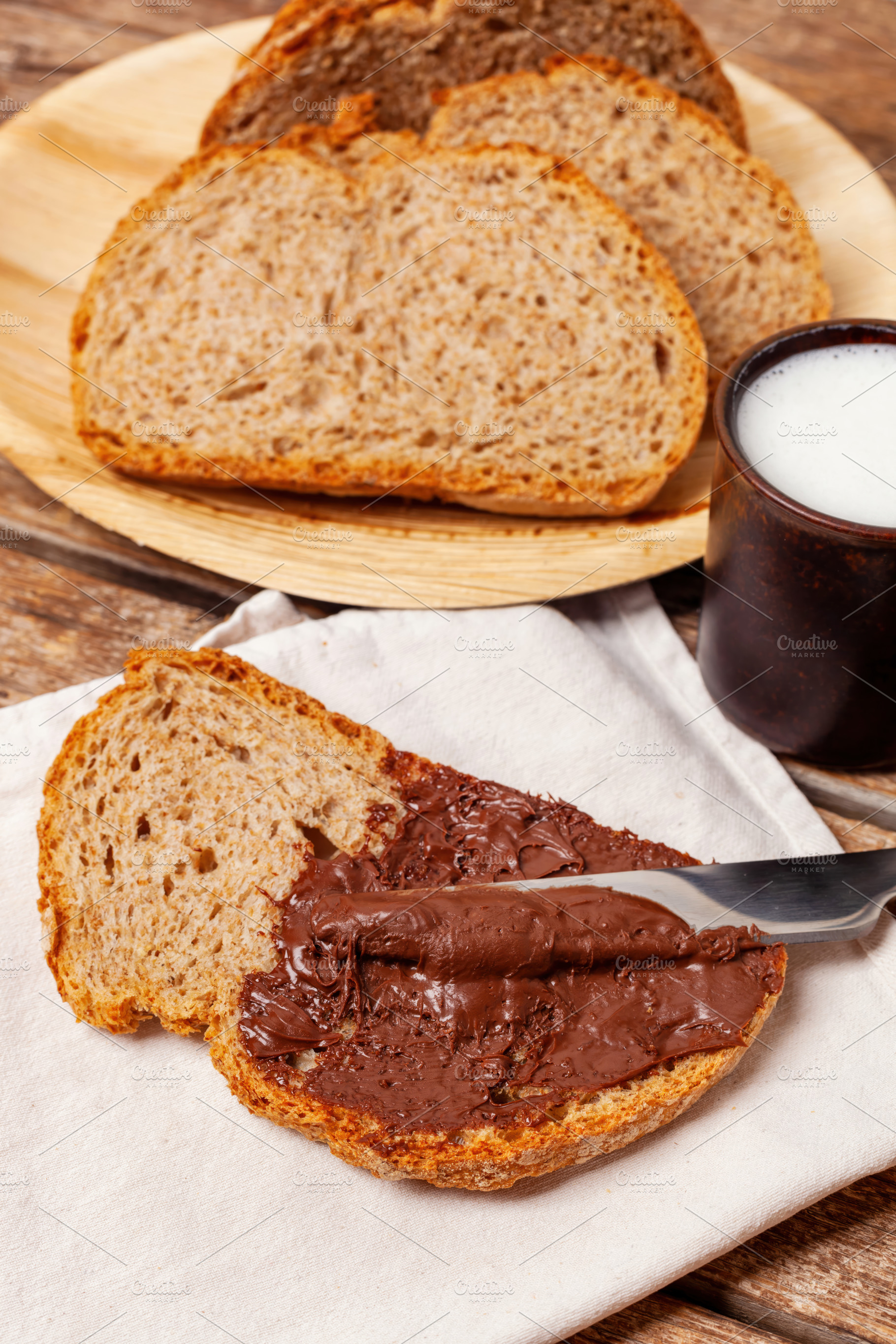 Spreading chocolate cream on a slice of whole wheat bread during breakfast, a Food & Drink Photo by Antonio Gravante Market