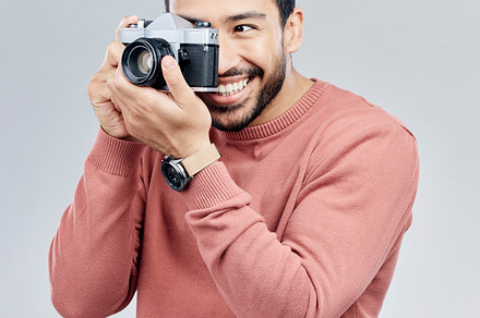 Man with camera, photography and happy with smile, taking picture with art isolated on studio background. Photographer, happiness and creativity with vintage technology with creative male artist, a Photo by Peopleimages.com
