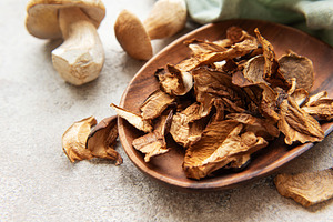 Dried porcini mushrooms resting in wooden bowl on gray textured, a Food & Drink Photo by Olena Rudo
