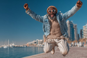 Excited individual joyfully jumping outdoors by a harbor on a sunny day, a Person Photo by AS photostudio