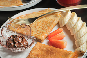 A plate of crepes filled with chocolate spread and topped with banana slices an, a Food & Drink Photo by Budarinphoto