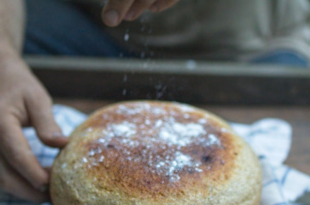 Baker's hand sprinkles flour on fresh bread close-up. A man finishes baking, de