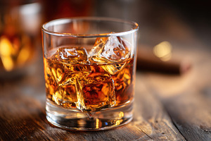 Glass of whiskey with ice on wooden table, a Food & Drink Photo by AlyaAnd