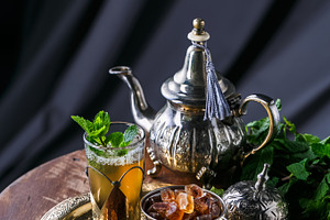 Glass of mint tea with dates and sugar on copper plate featuring moroccan