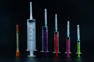 A composition of various size syringes on a dark background, highlighting theme, a Health & Medical Photo by Rohan Photography