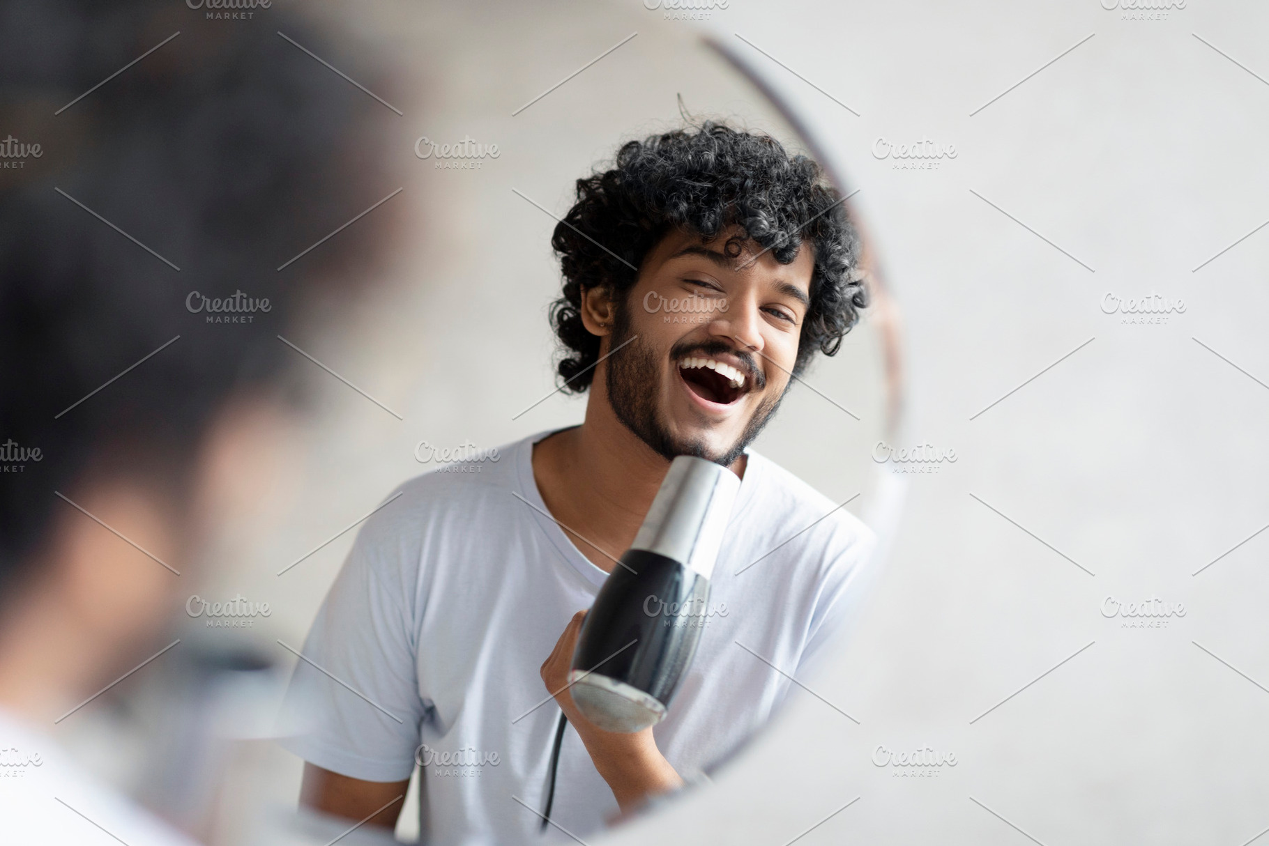 Joyful indian man holding hairdryer and singing as in microphone, having fun wh, a Person Photo by Prostock-Studio