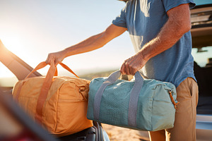 Man loading travel bags into car at sunset, a Holiday Photo by AlyaAnd