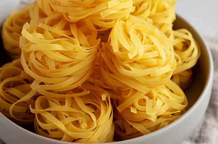 Raw Dry Tagliatelle Pasta in a Bowl, side view., a Food & Drink Photo by LiudmylaChuhunova