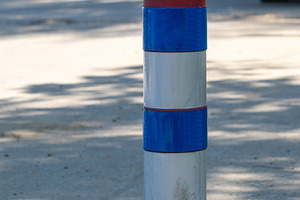 Vertical blue and white striped traffic bollard on pavement, with blurred parke, a Holiday Photo by Ales Munt