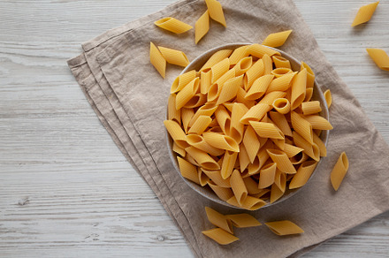 Raw Organic Dry Pennoni Pasta in a Bowl, top view. Copy space., a Food & Drink Photo by LiudmylaChuhunova