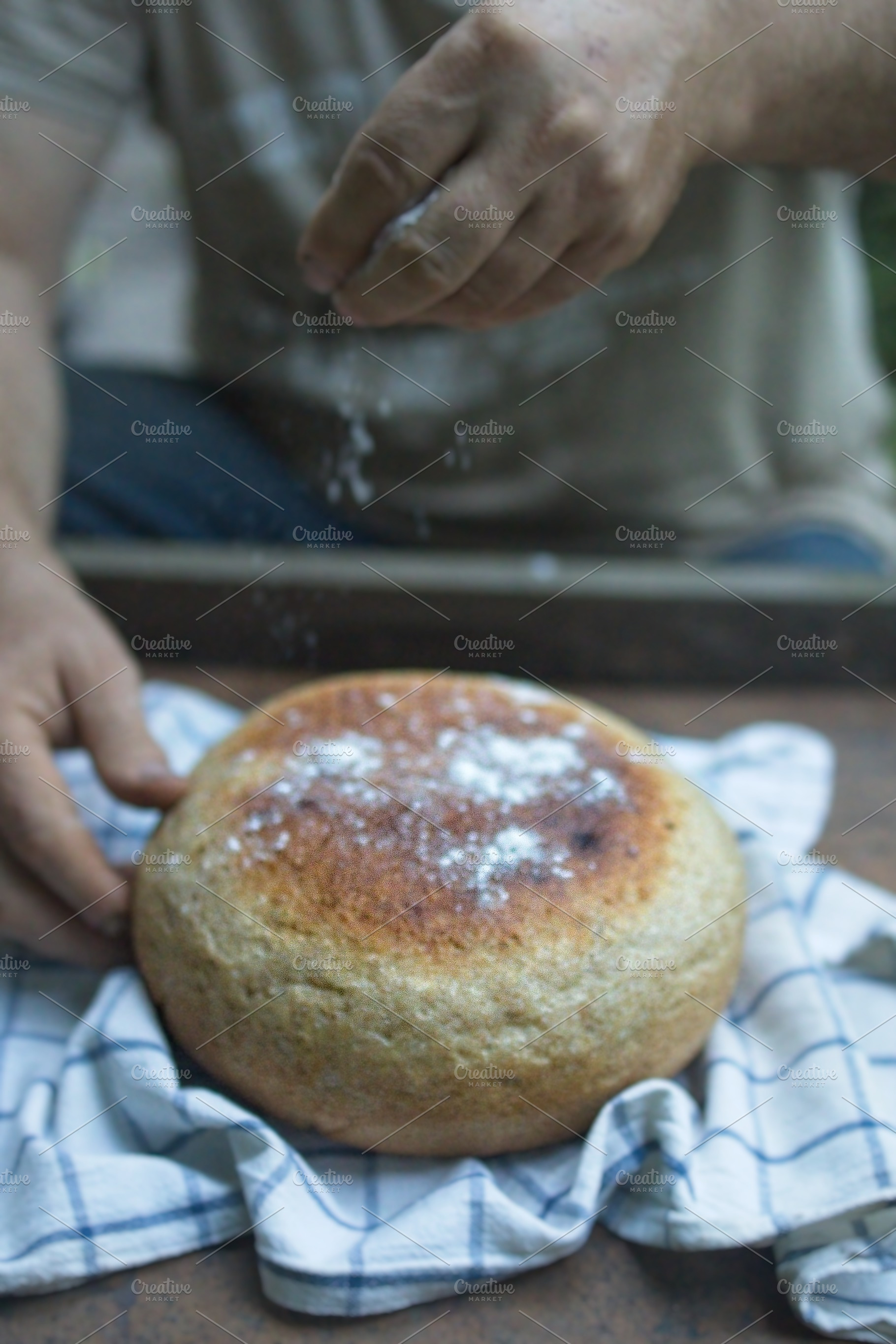 Baker's hand sprinkles flour on fresh bread close-up. A man finishes baking, de, a Food & Drink Photo by TanaCh