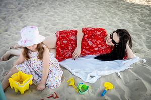 Mother relaxing on a towel on the beach while her daughter plays, a Person Photo by Imaginarium