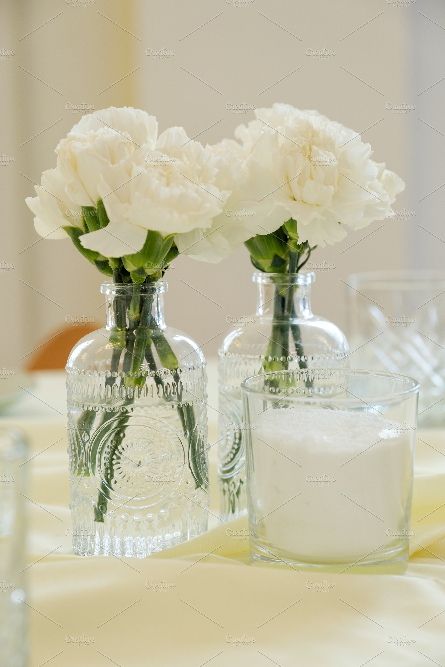 Elegant white carnations in decorative vintage glass bottles on table., a Food & Drink Photo by Rohan Photography