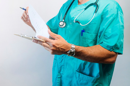 Focused male doctor reviewing documents on clipboard, wearing scrubs and stetho