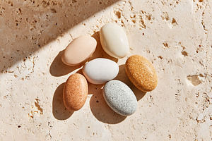 Colorful oval and round stones arranged on textured surface in natural sunlight, a Photo by AlyaAnd