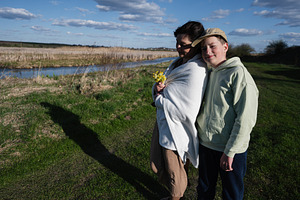Mother and son wrapped in a blanket by the riverside holding yellow wildflowers, a Person Photo by AS photostudio