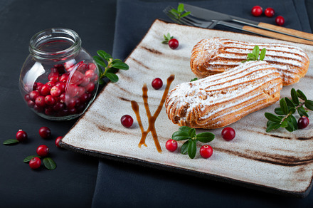 Cream eclairs choux pastries served with fresh cranberries on a