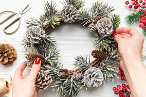 Hands decorating christmas wreath with pine cones and evergreen, a Holiday Photo by Olena Rudo