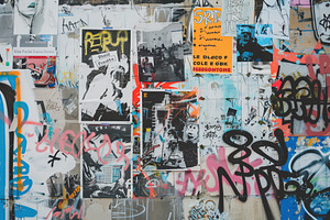 A Vibrant Urban Wall Covered In A Collage Of Posters And Graffiti. The Artwork