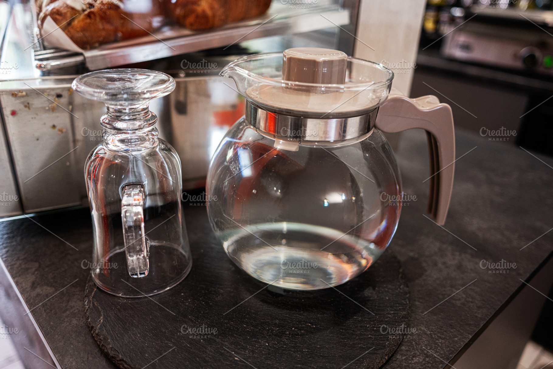 Clear glass pitcher and inverted mug on a dark countertop with pastries nearby, a Photo by AS photostudio