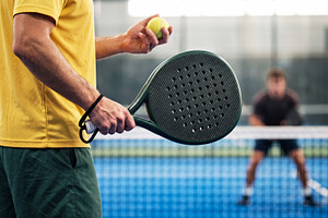 Close up of male padel player preparing to serve ball on court.