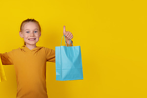 Smiling young girl holding yellow and blue shopping bags, standi, a Person Photo by Ales Munt