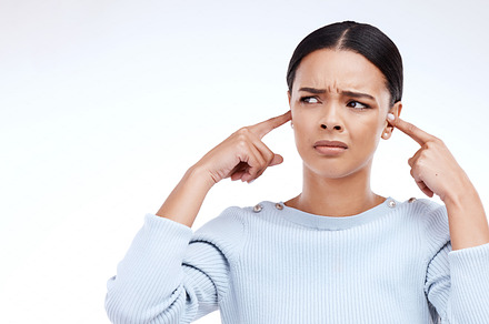 Annoyed, woman and finger in ears for noise, loud and denial gesture on studio white background. Omg, face and angry girl with complaint, ignoring and deaf, wtf and emoji, frustrated and unhappy, a Photo by Peopleimages.com
