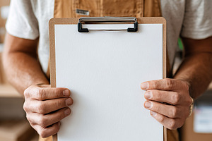 Man in brown overalls holds blank clipboard in storage facility while preparing, a Photo by AlyaAnd