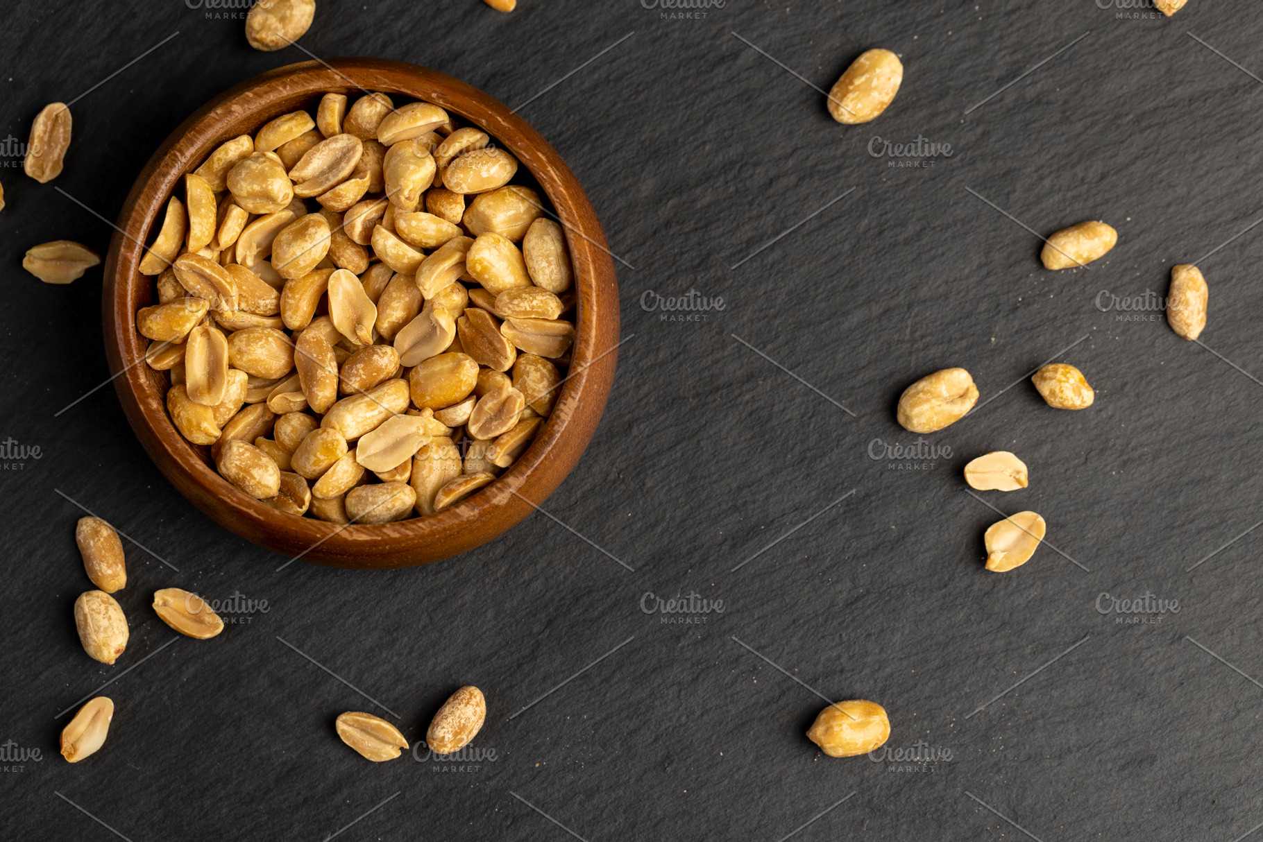 peanuts in a wooden bowl, crunchy peanuts without shells on a black slate board, a Photo by rsoollAI