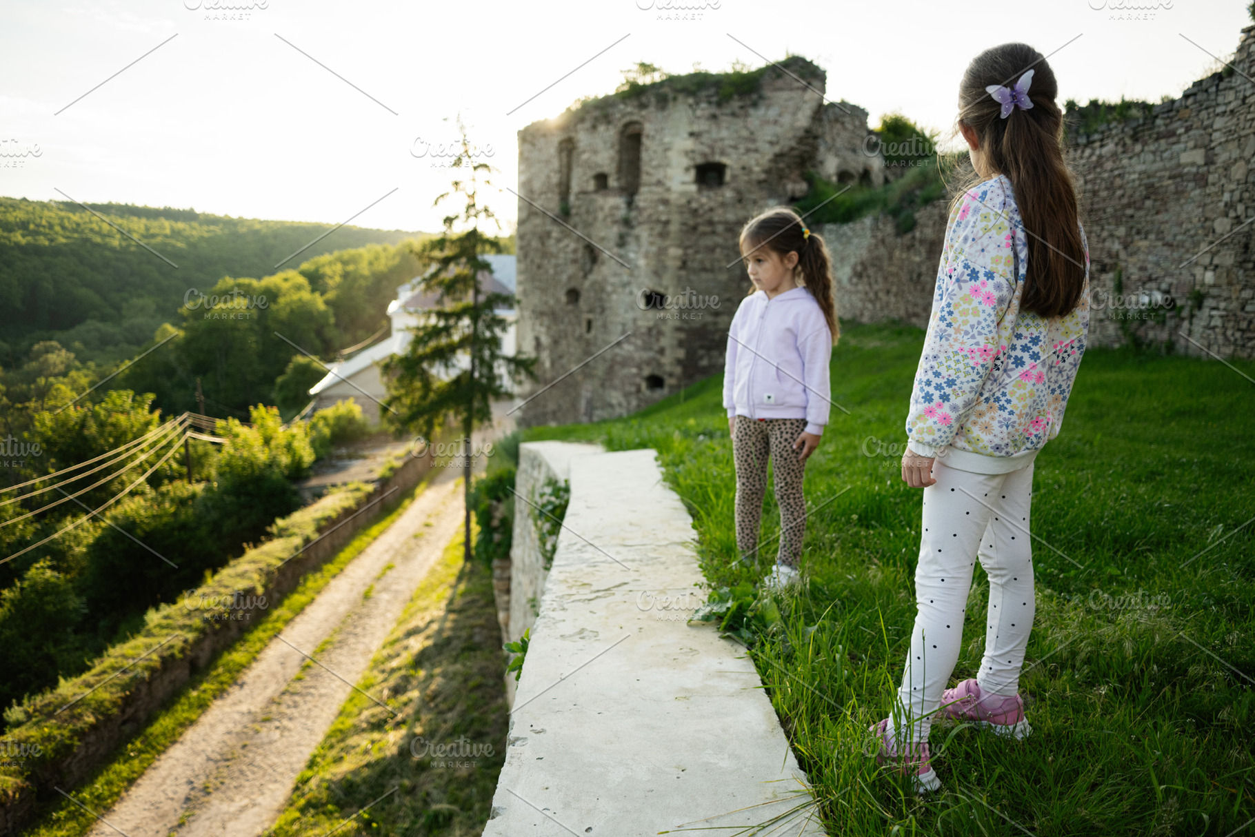 Two girls exploring an old castle with scenic nature views at sunset, a Person Photo by AS photostudio