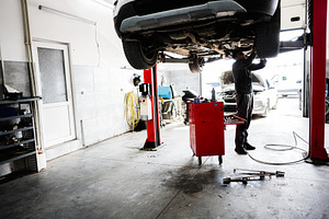 Mechanic working under car in a vehicle garage workshop maintenance environment, a Transportation Photo by AS photostudio