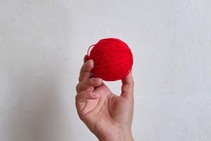 A person holding a red ball of wool yarn in their hand against a