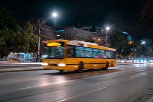 A vibrant yellow bus speeds through a city street at night, illuminated by stre, a Business Photo by ImageMir