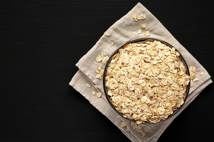Wholegrain Oat Flakes in a Bowl on a black background, top view., a Food & Drink Photo by LiudmylaChuhunova