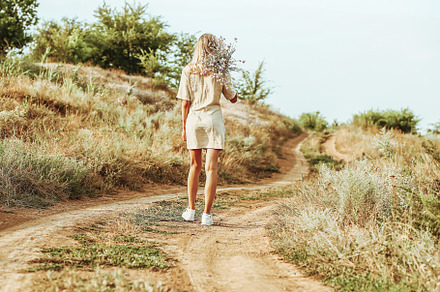 A girl with a bouquet of autumn flowers walks along an autumn road with her bac