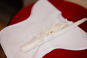 White decorated christening candle on embroidered cloth with ribbon and pearls, a Photo by AS photostudio