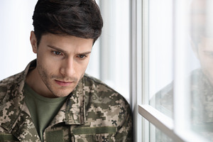 depressed military guy standing next to window, closeup, a Photo by Prostock-Studio