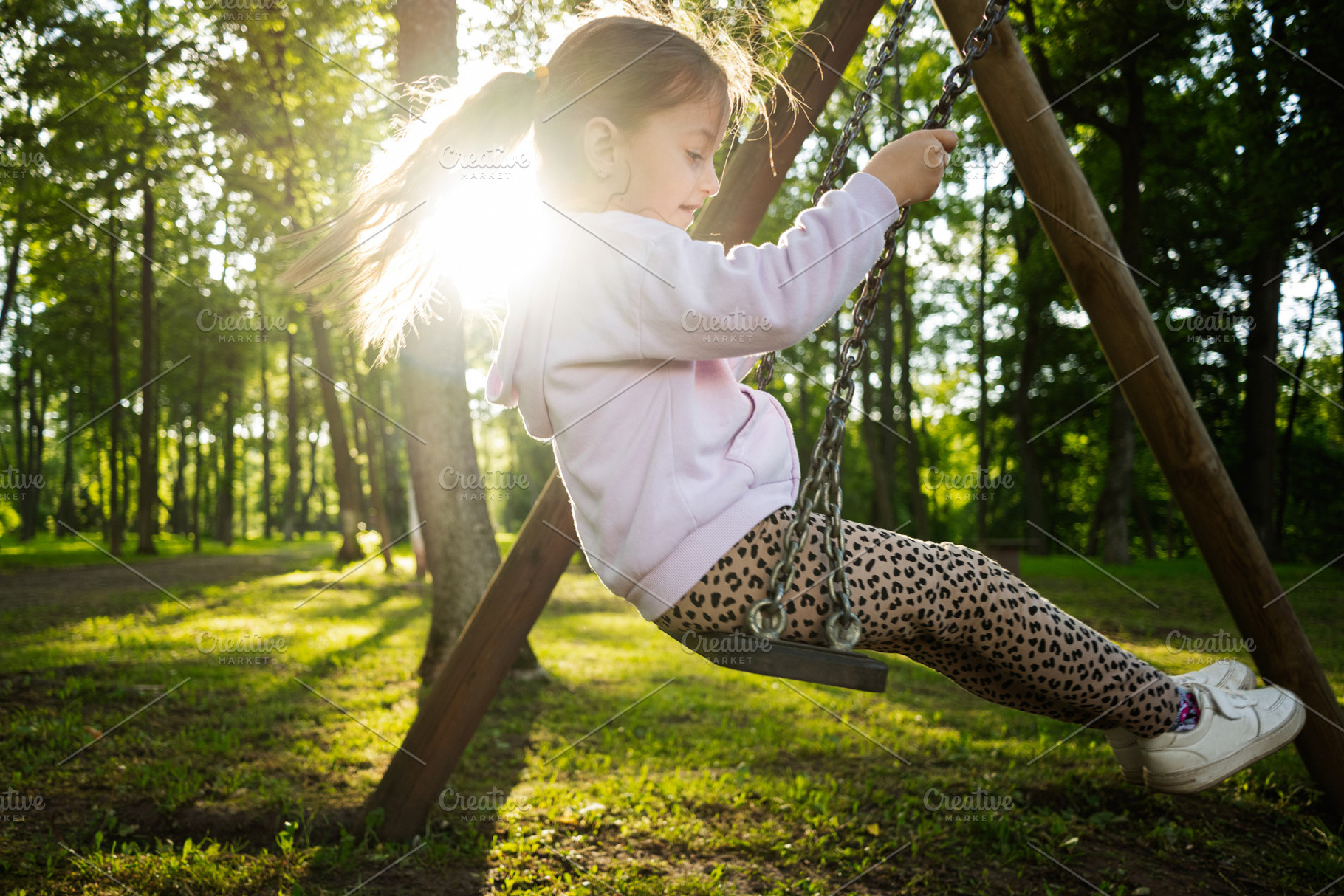 Girl enjoying a sunny day on a swing in a lush park, a Photo by AS photostudio