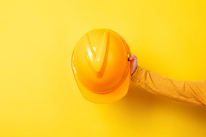 Hand holding a yellow construction helmet against a matching yel, an Industrial Photo by Ales Munt