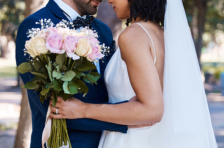 Wedding, couple and marriage outdoor with commitment, trust and love with bride and groom in park. Life partner, married man and black woman with rose bouquet, content and interracial relationship, a Photo by Peopleimages.com