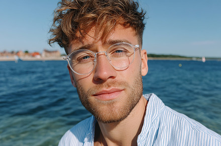 Young man in glasses smiling at camera by the water on a sunny day, a Person Photo by AlyaAnd