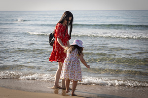 Mother and daughter walking barefoot by the sea on the sand, enj, a Person Photo by Imaginarium